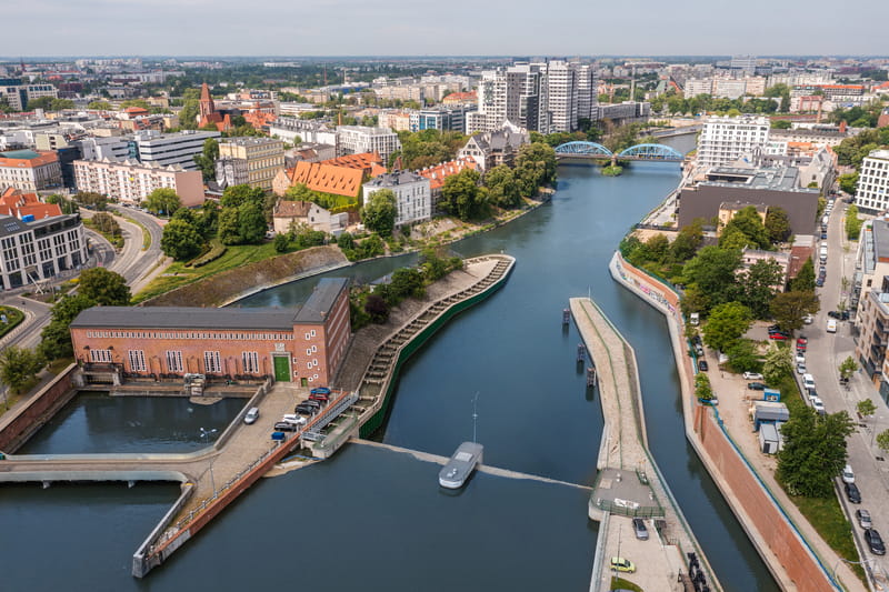 Zdjęcie przedstawia widok z lotu ptaka na elektrownię wodną Wrocław 1, z pejzażem miasta.